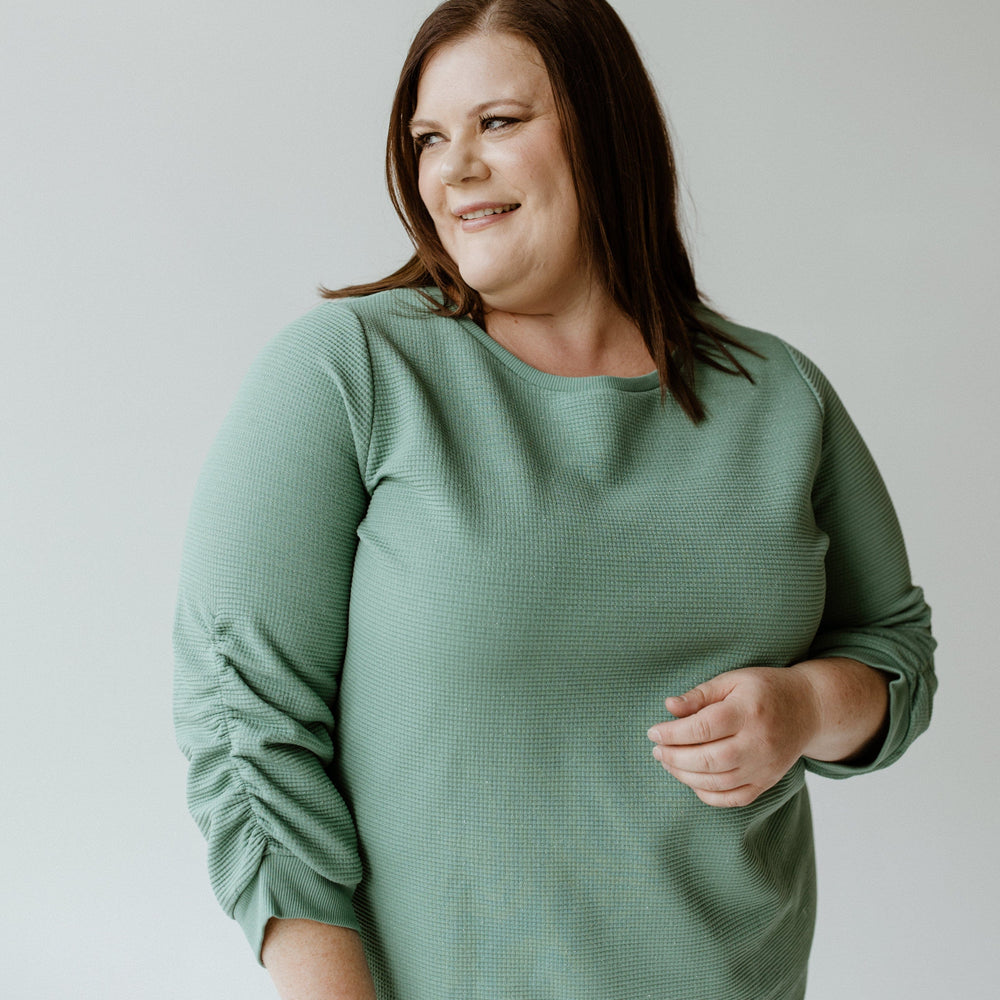 A person wearing the Yesta Thermal Sparkle 3/4 Tee in Frosted Juniper with jeans stands against a plain background, looking to their left with a slight smile.