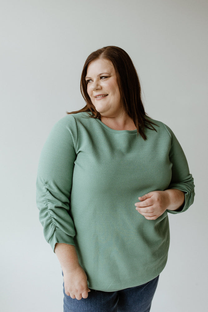 A person wearing the Yesta Thermal Sparkle 3/4 Tee in Frosted Juniper with jeans stands against a plain background, looking to their left with a slight smile.