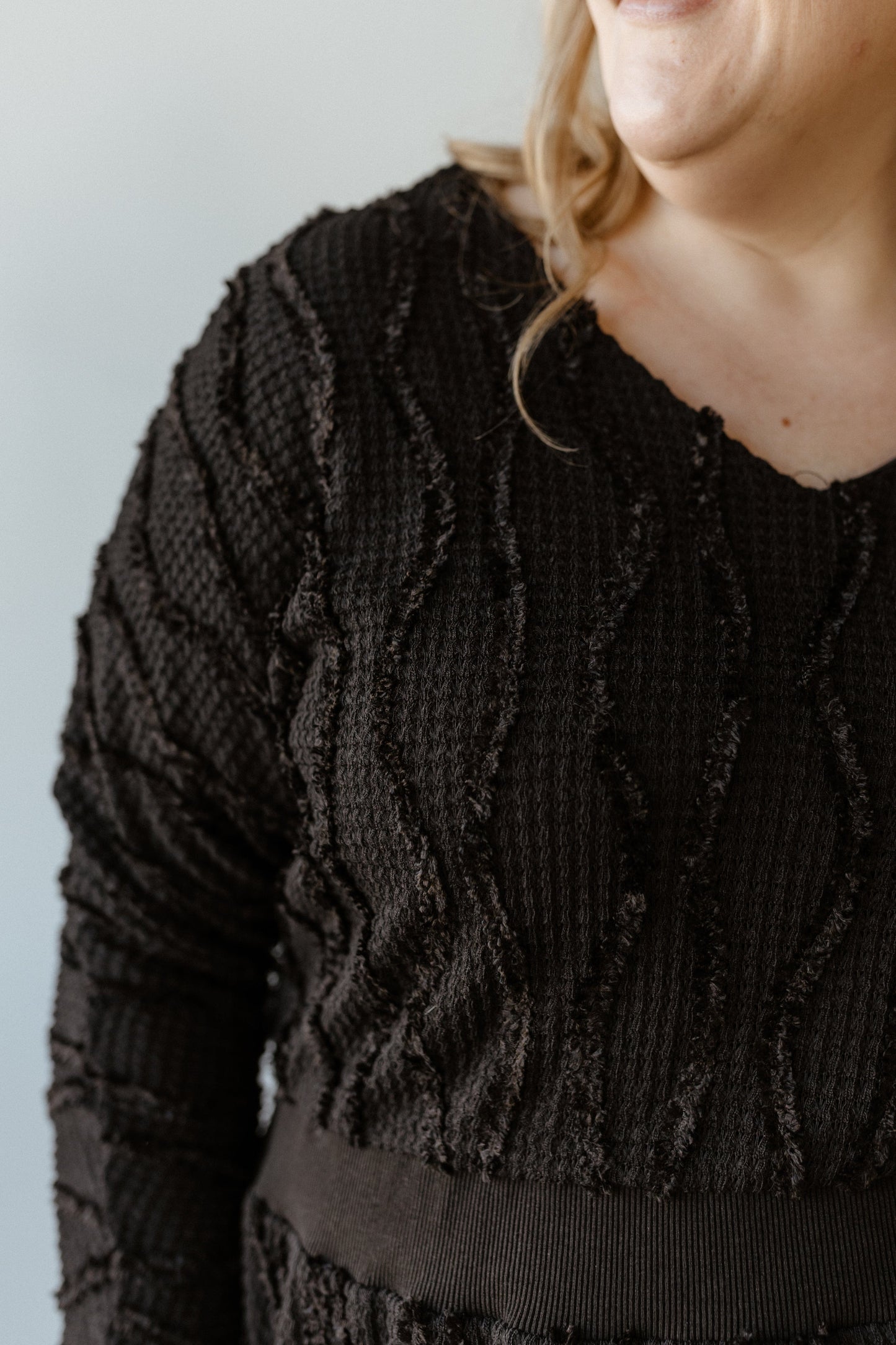 A person wearing a black sweater with a wave pattern, reminiscent of the cozy vibe of a thermal texture dress, stands against a light gray background.