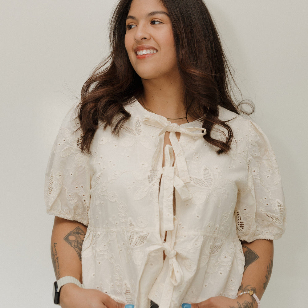 Woman wearing a white blouse with lace details against a plain background