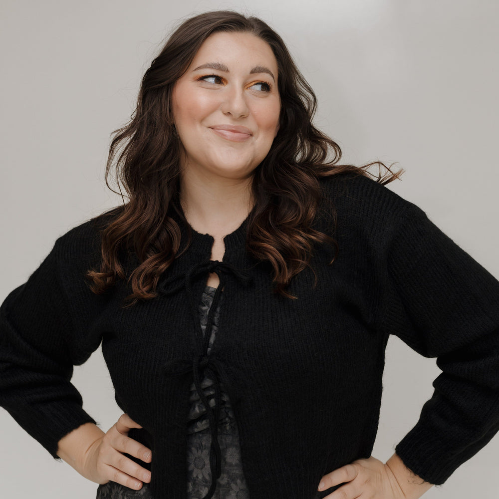 Woman wearing a black cropped jacket and patterned skirt against a plain background