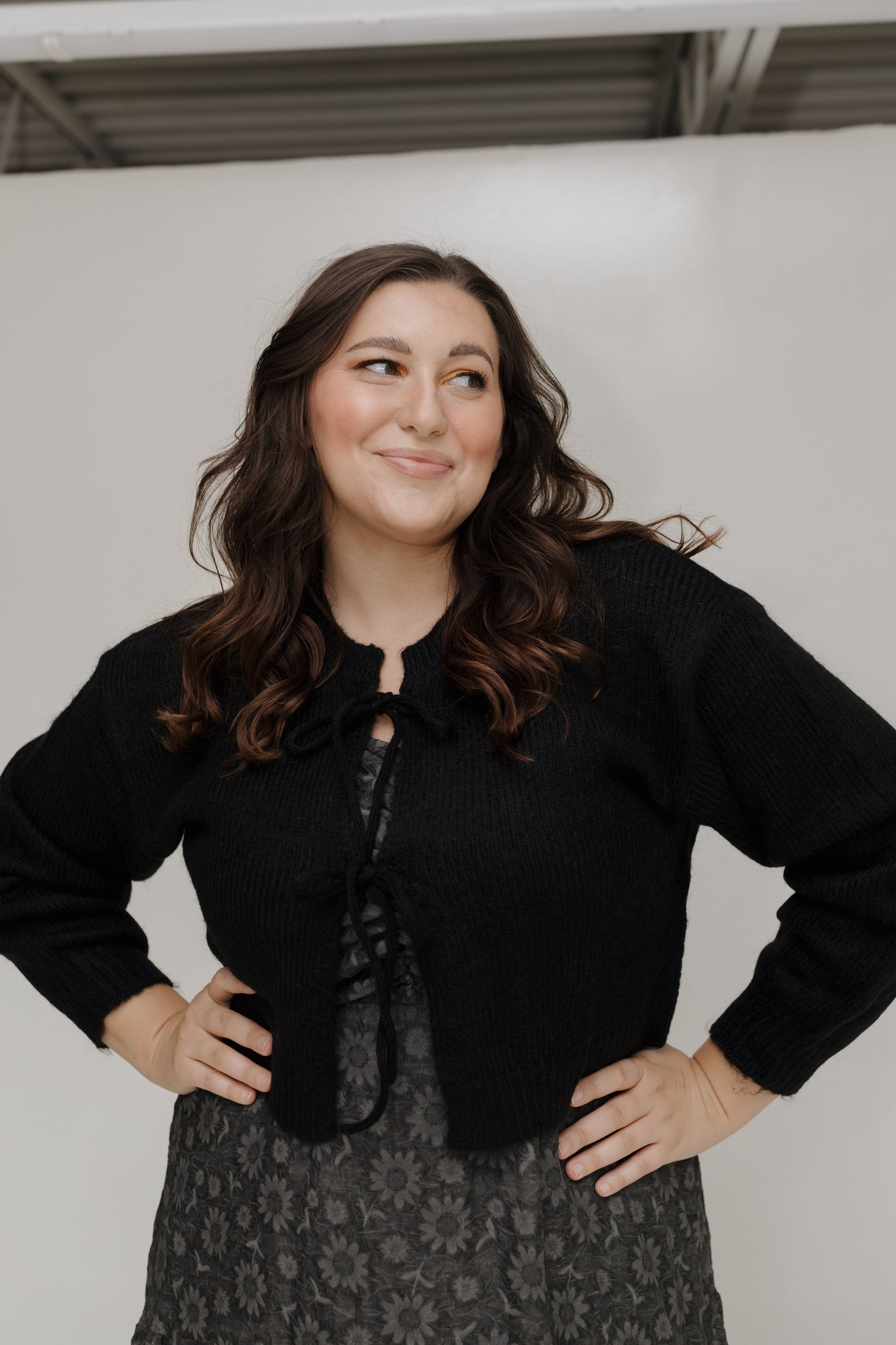 Woman wearing a black cropped jacket and patterned skirt against a plain background