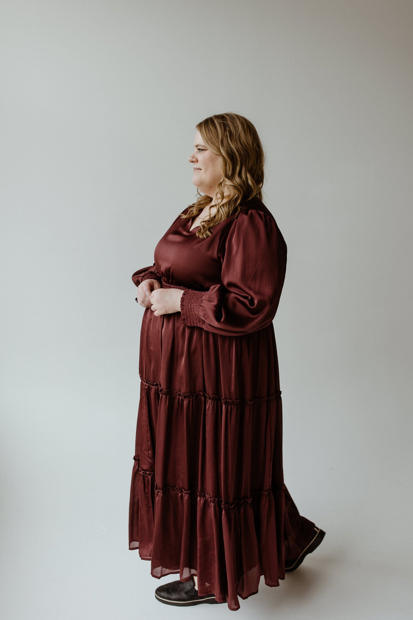 A person in a Zinfandel blouson dress with a smocked waist stands against a plain background, looking to the side.