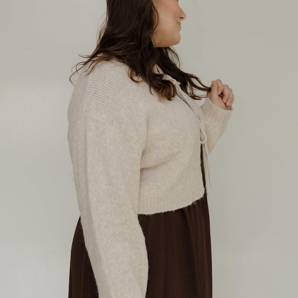 Woman wearing a beige sweater over a brown dress against a white background