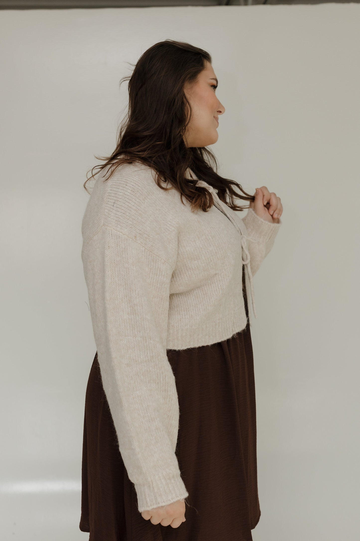 Woman wearing a beige sweater over a brown dress against a white background