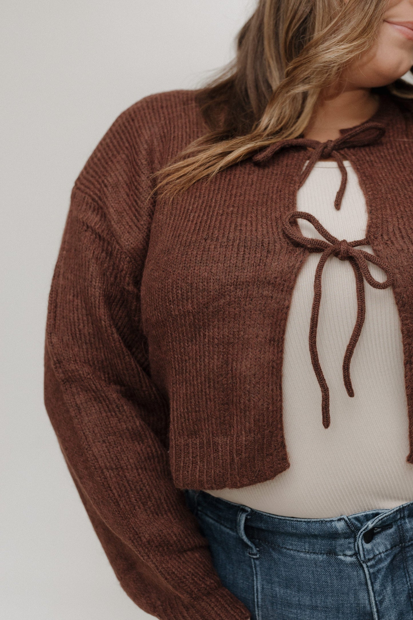 Brown ribbed sweater with a bow detail worn by a person on a plain background