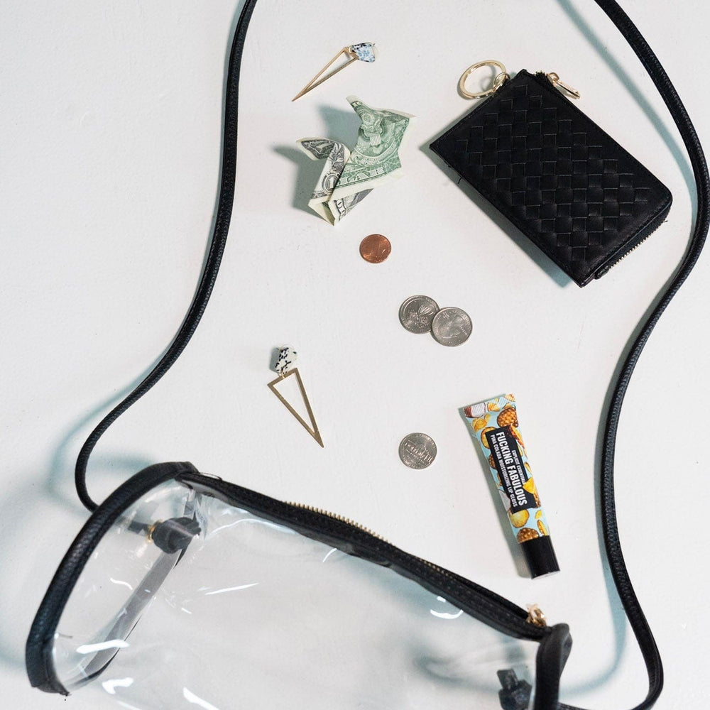 Clear pouch with black strap, wallet, coins, cards, and small items on a white background