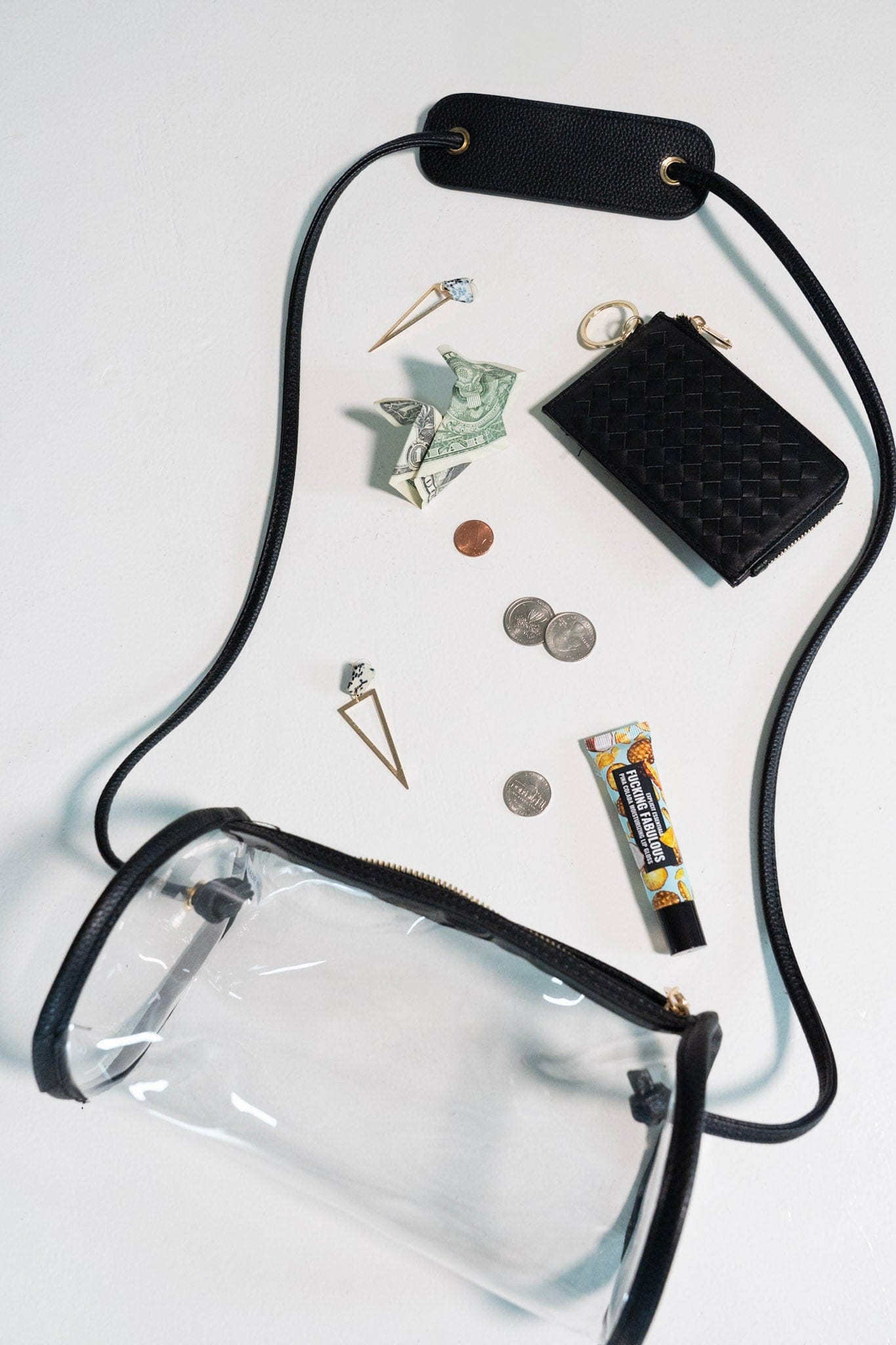 Clear pouch with black strap, wallet, coins, cards, and small items on a white background