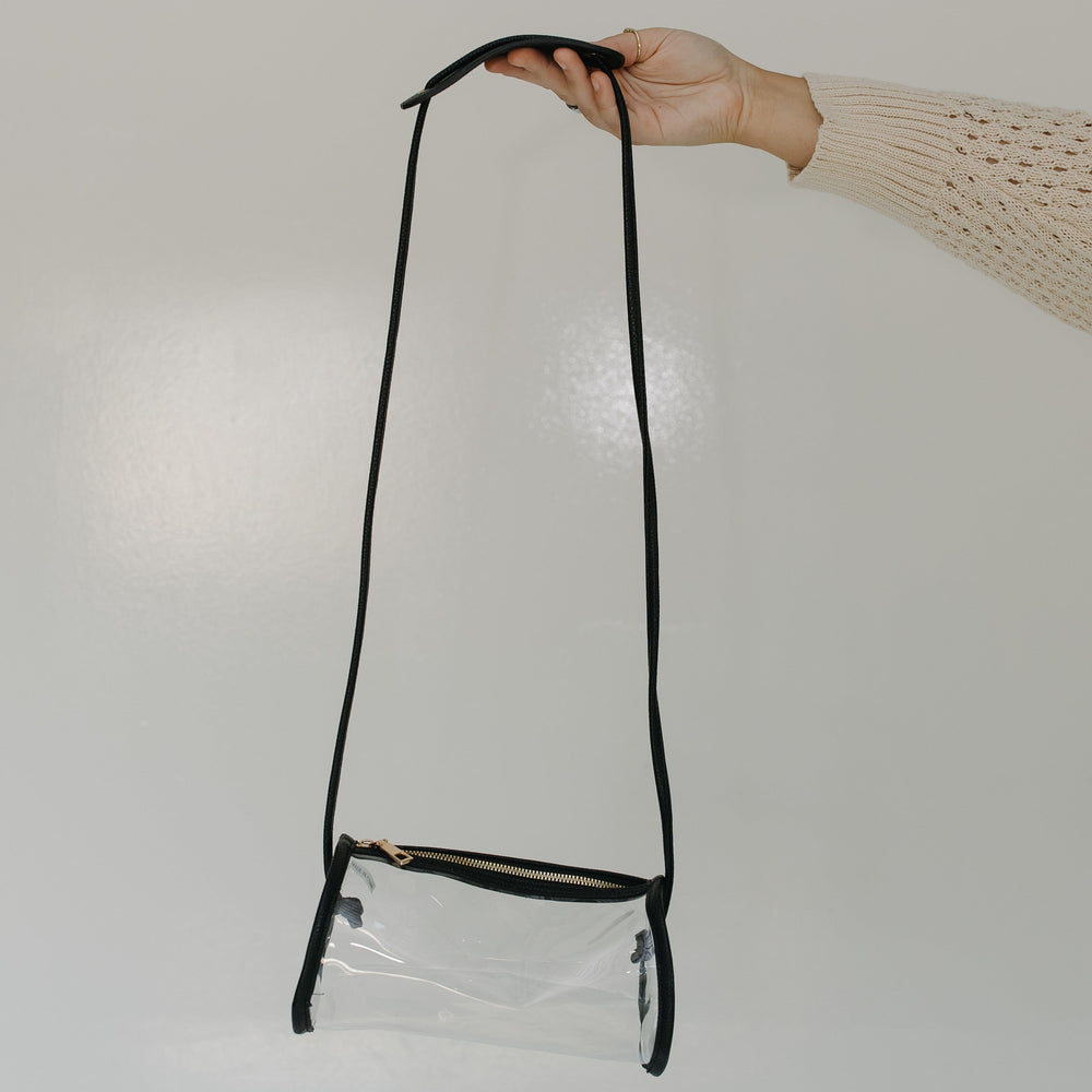 Clear crossbody bag with black strap held by a hand on a white background