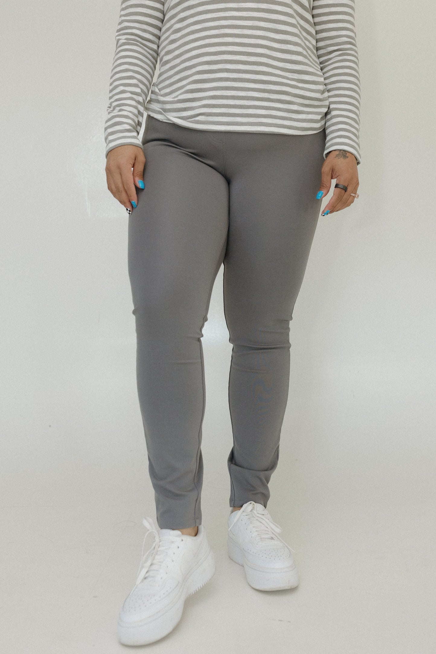 Person wearing gray jogger pants and a striped shirt on a plain background