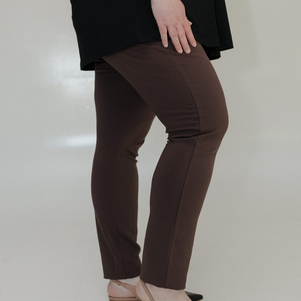 Person wearing brown pants and black shoes on a plain background