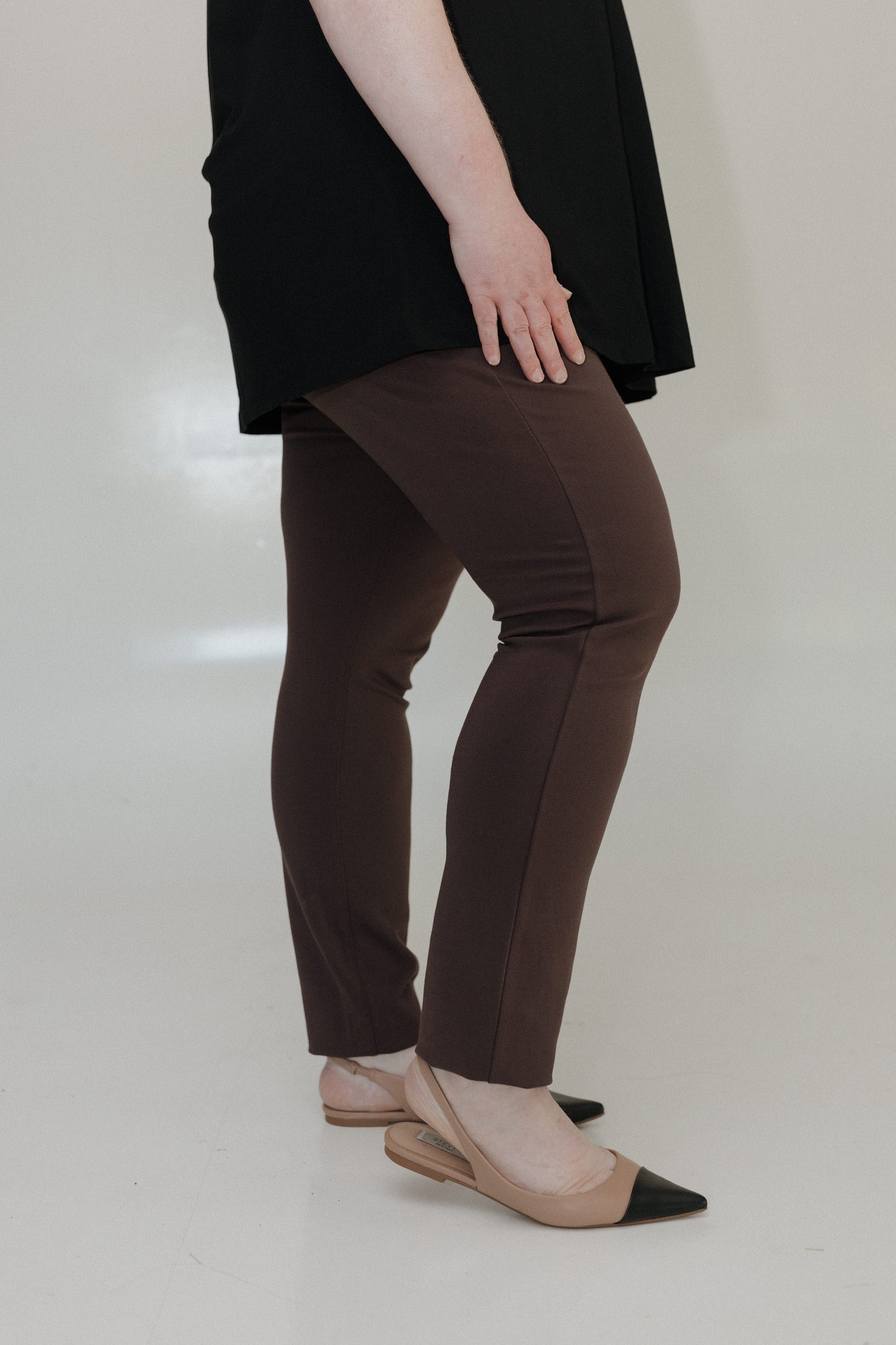 Person wearing brown pants and black shoes on a plain background