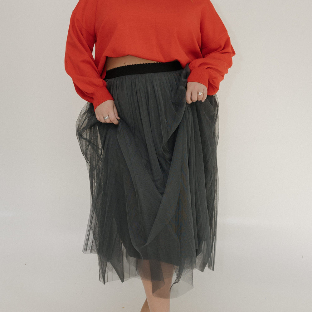 Person wearing a red sweater and black tulle skirt on a plain background