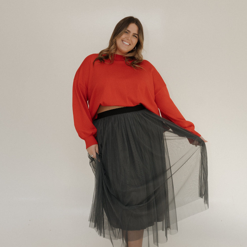 Woman wearing a red sweater and black tulle skirt against a white background