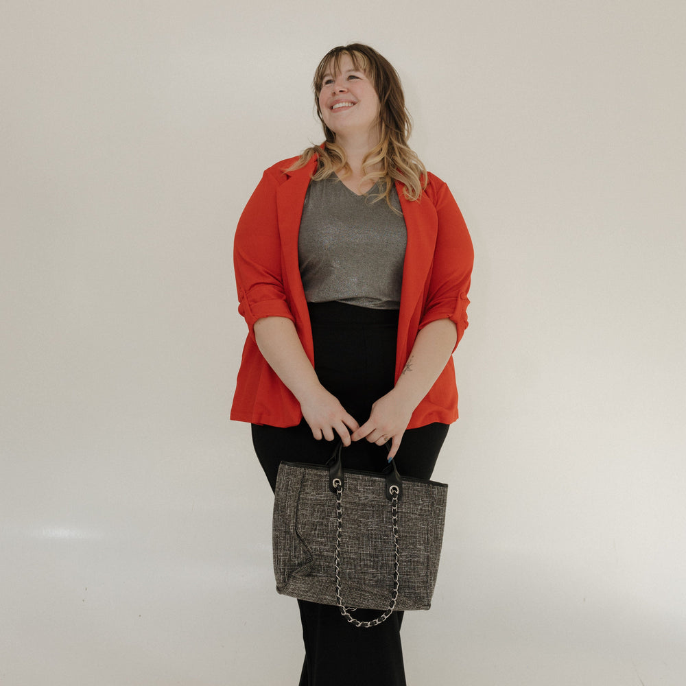 Woman wearing a red jacket and black pants holding a gray bag against a white wall.