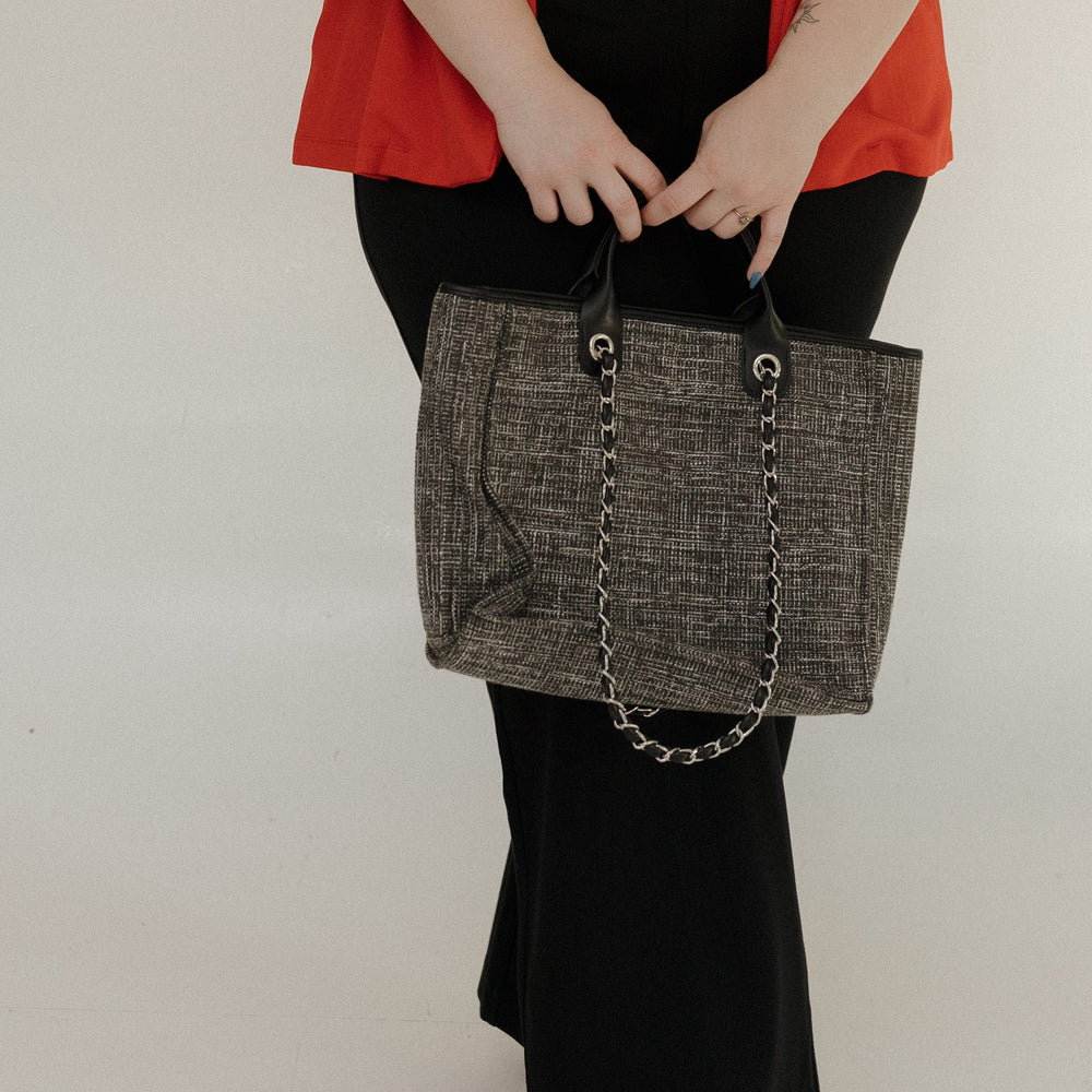 Person holding a gray textured handbag with a chain detail against a plain background