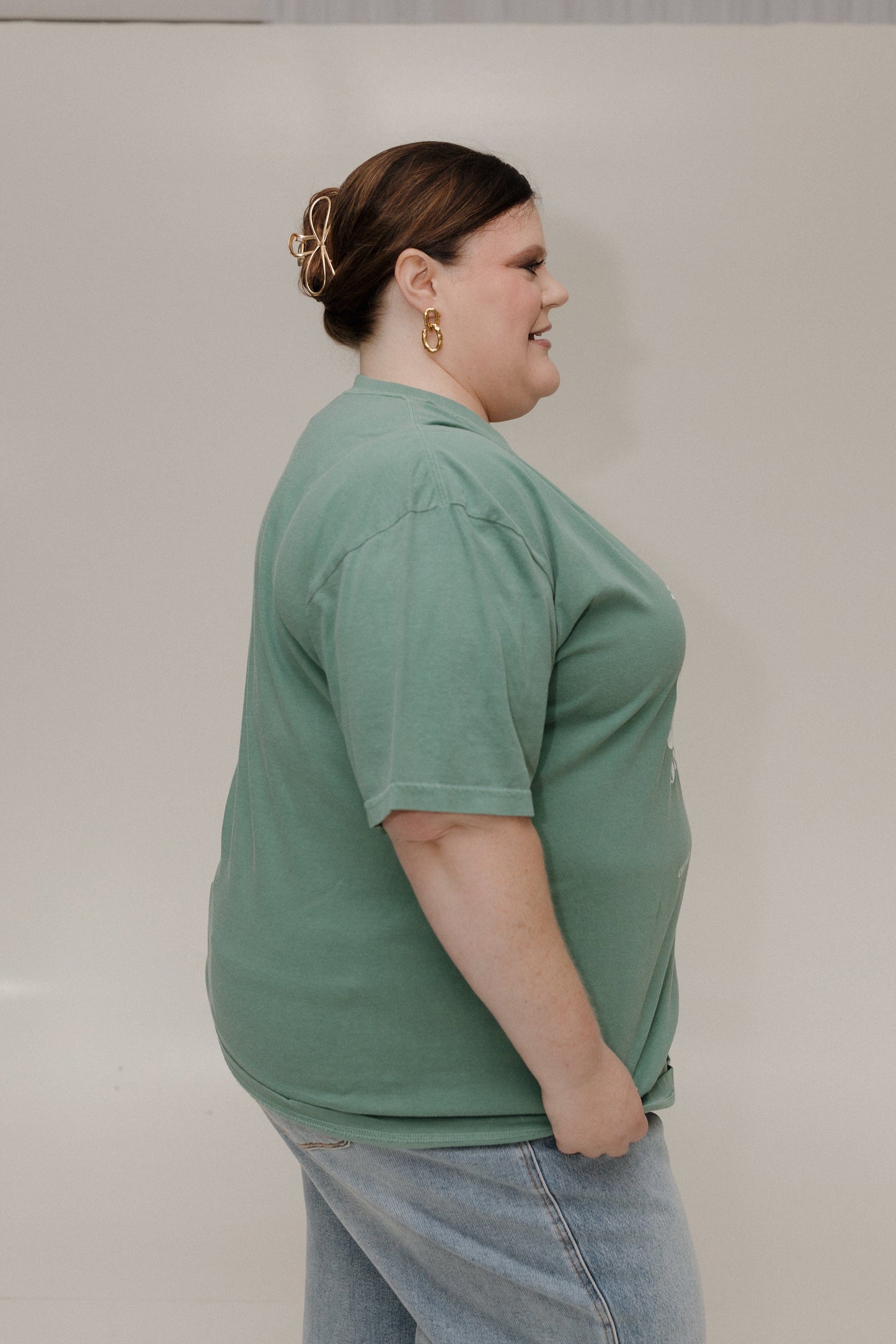 Person wearing a green shirt and light blue jeans against a plain background