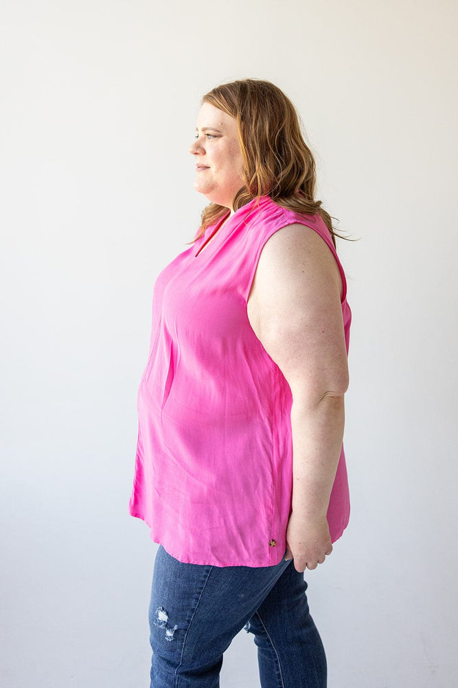 A person with shoulder-length hair wearing a bright pink V-NECK FLOWY TANK BLOUSE WITH RUCHED SHOULDER IN FRESH FUCHSIA by Love Marlow and blue jeans stands in profile against a plain white background, epitomizing effortless summer fashion.