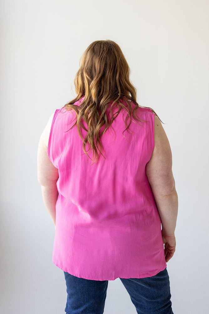 A person with long, wavy hair is shown from the back, wearing a sleeveless **Love Marlow V-NECK FLOWY TANK BLOUSE WITH RUCHED SHOULDER IN FRESH FUCHSIA** and dark blue jeans against a plain background.