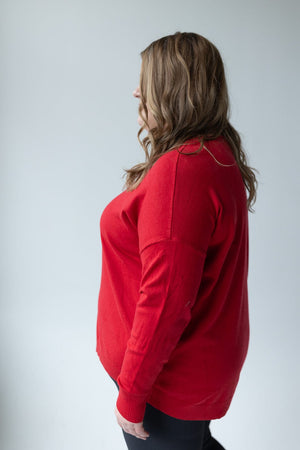 A person in the Zenana V-Neck Front Seam Sweater in red paired with black pants stands sideways against a plain background, showcasing the soft fabric's blend of style and comfort.