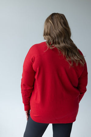 A person with long hair is wearing the Zenana V-Neck Front Seam Sweater in red and black pants, facing away from the camera against a light gray background.