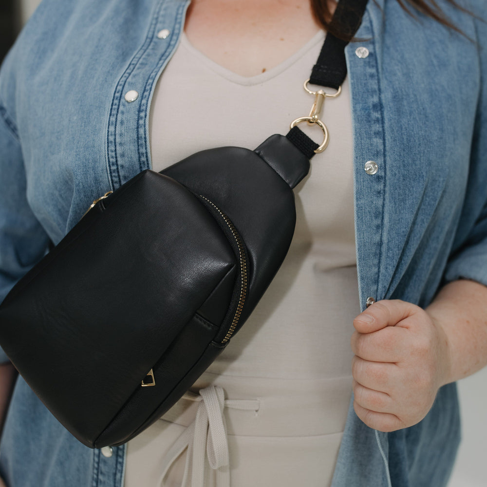 Person wearing a black sling bag over one shoulder with a neutral background