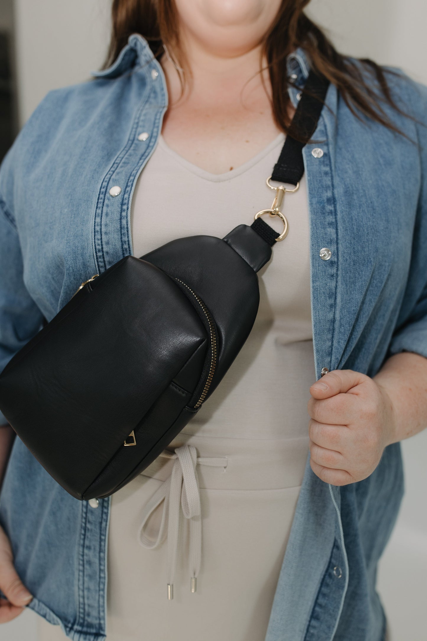 Person wearing a black sling bag over one shoulder with a neutral background