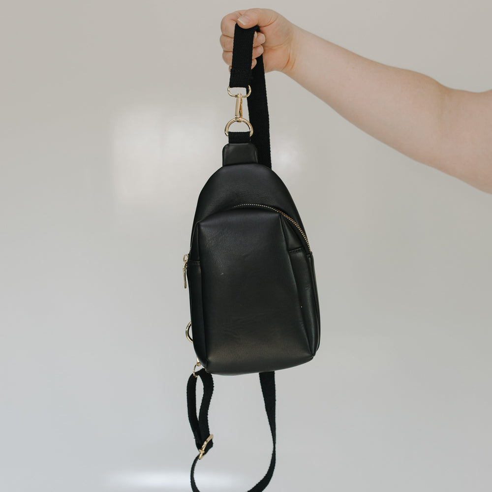 Black leather crossbody bag held by a hand against a neutral background