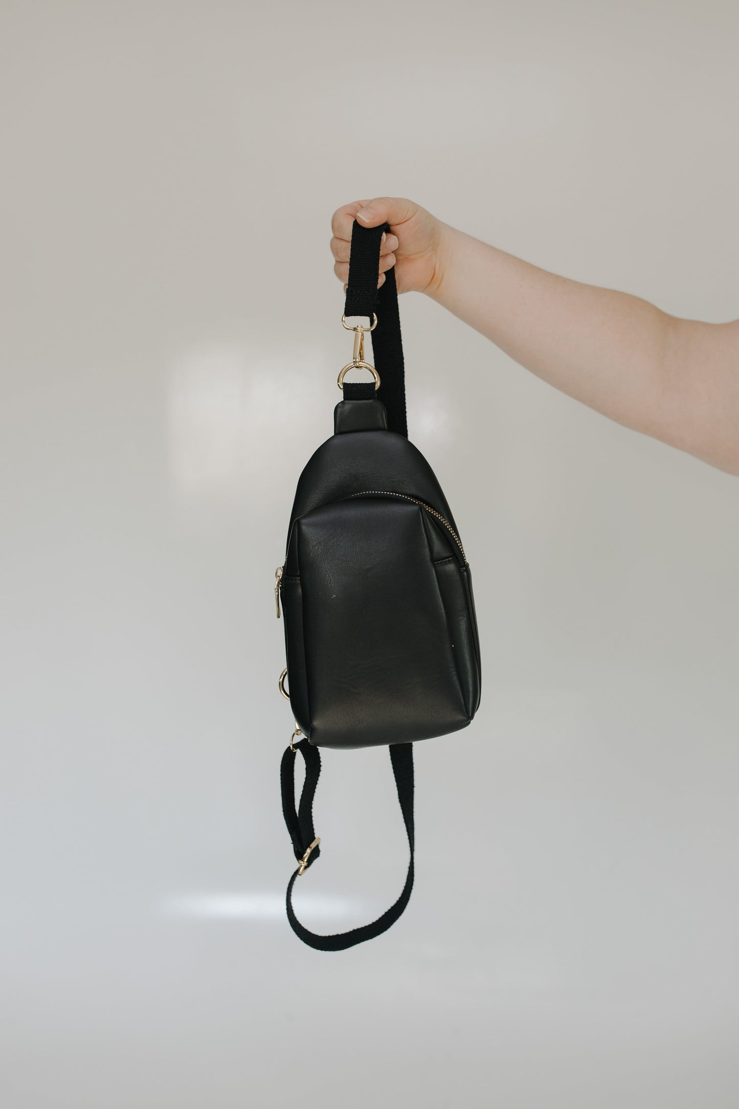 Black leather crossbody bag held by a hand against a neutral background