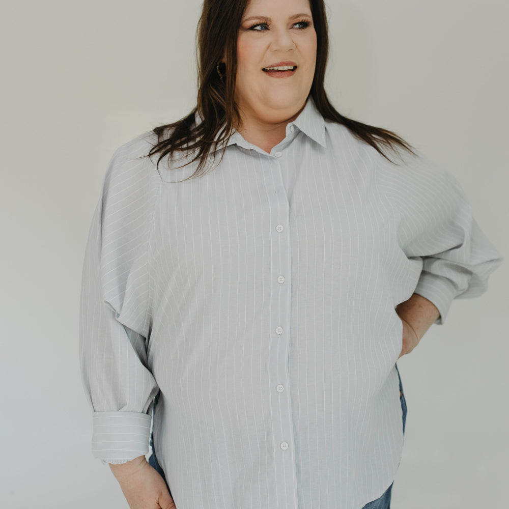 Woman wearing a light gray button-up shirt and blue jeans against a plain background