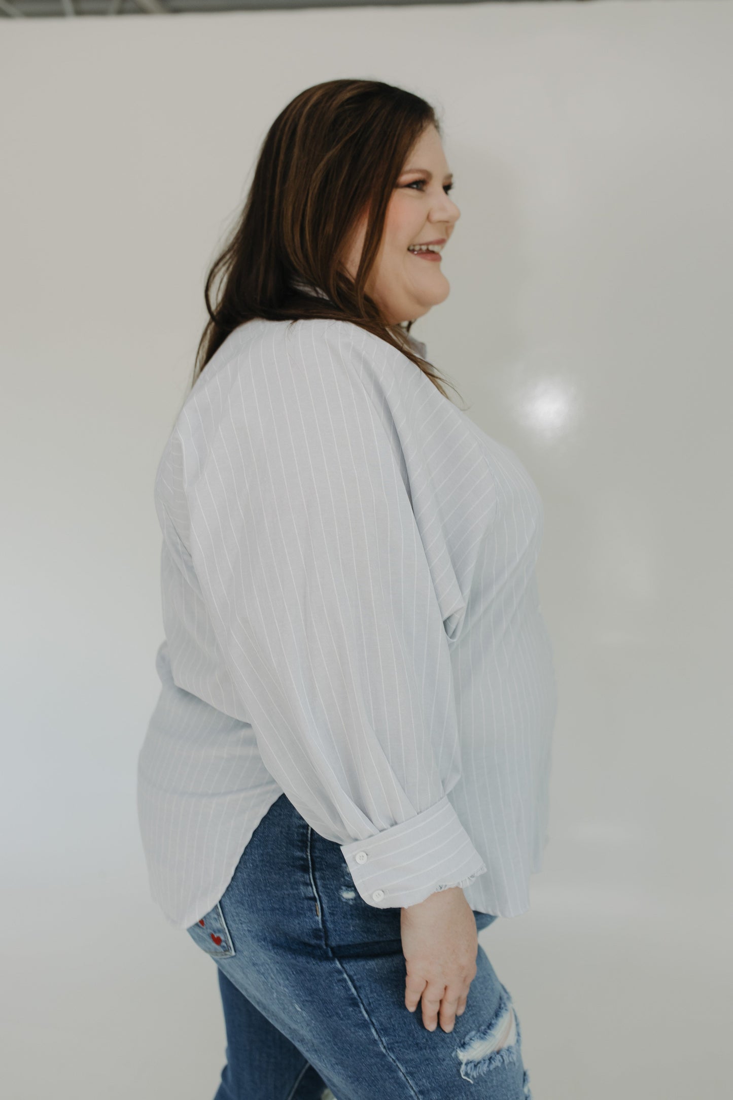 Woman wearing a light gray sweater and blue jeans against a white background