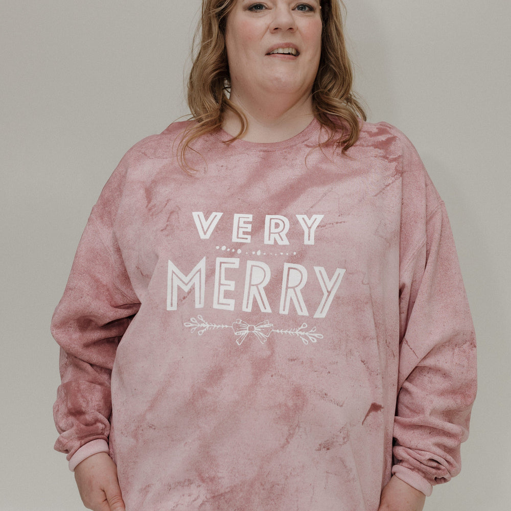 Person wearing a pink 'Very Merry' sweater against a plain background