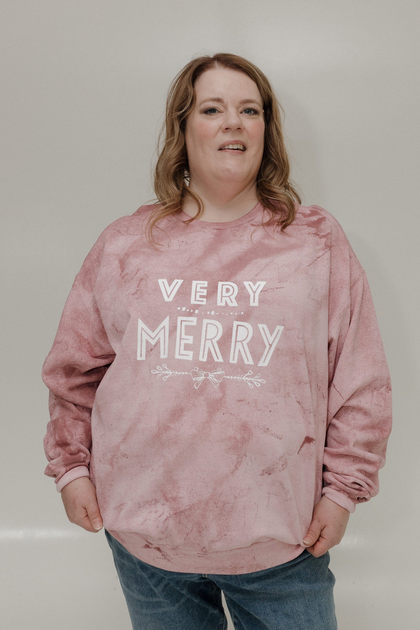 Person wearing a pink 'Very Merry' sweater against a plain background