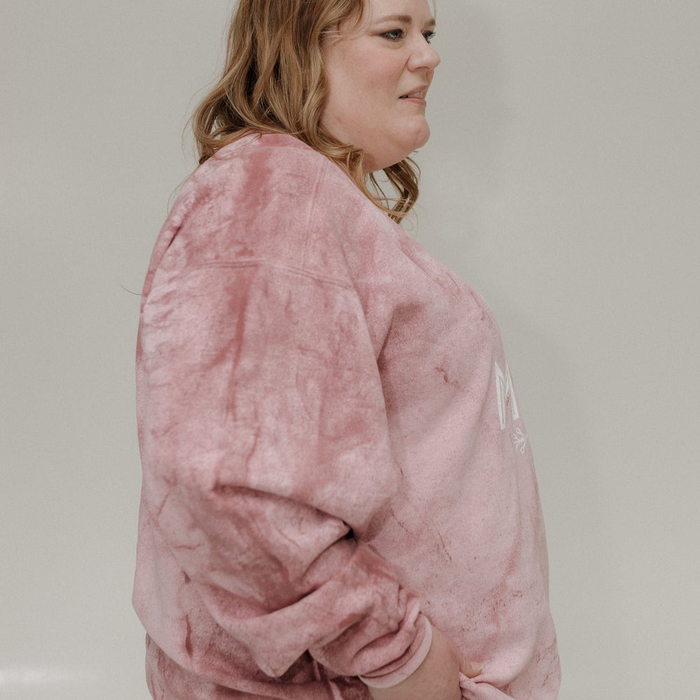 Person wearing a pink tie-dye sweatshirt and blue jeans against a plain background