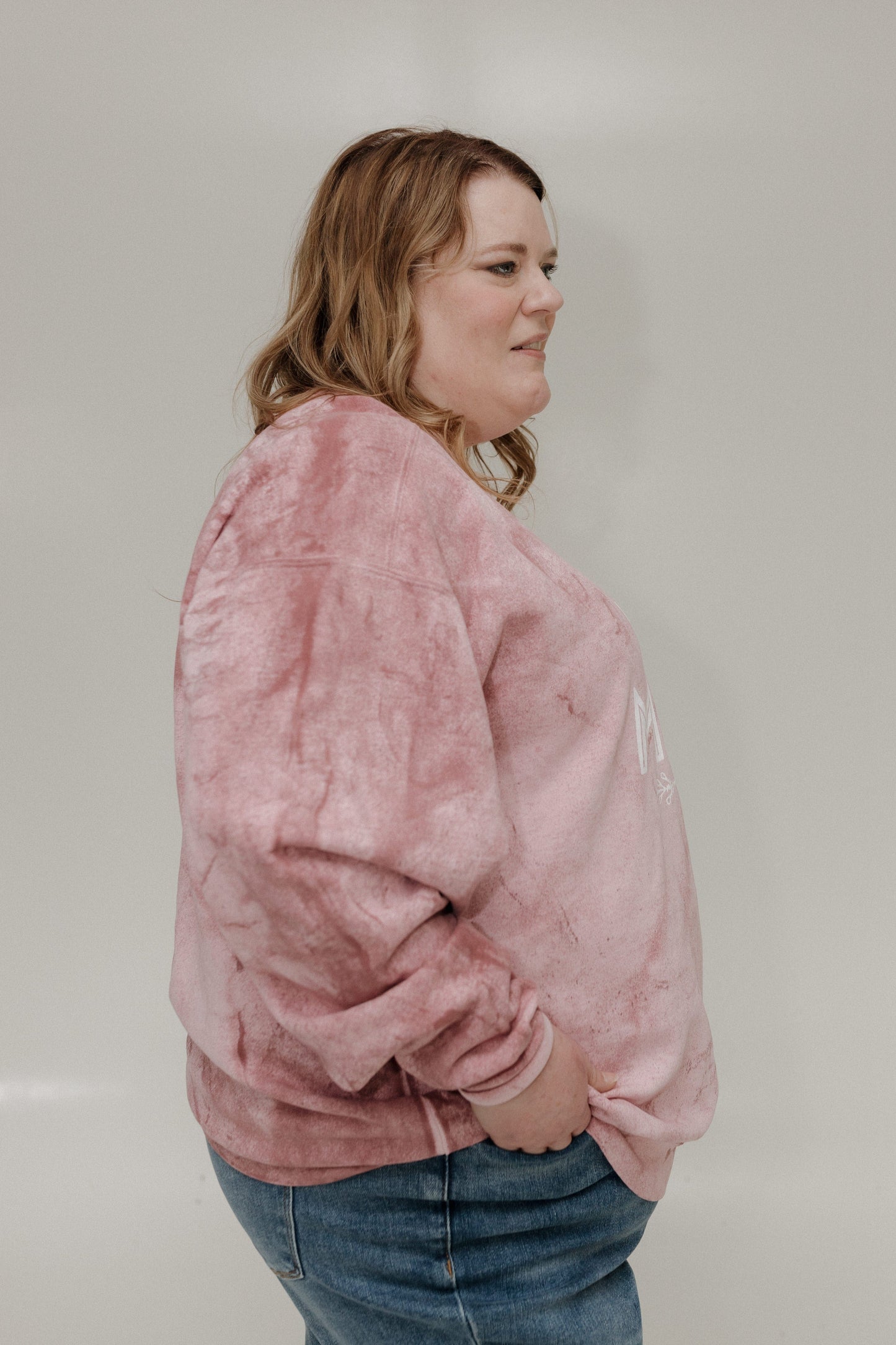 Person wearing a pink tie-dye sweatshirt and blue jeans against a plain background