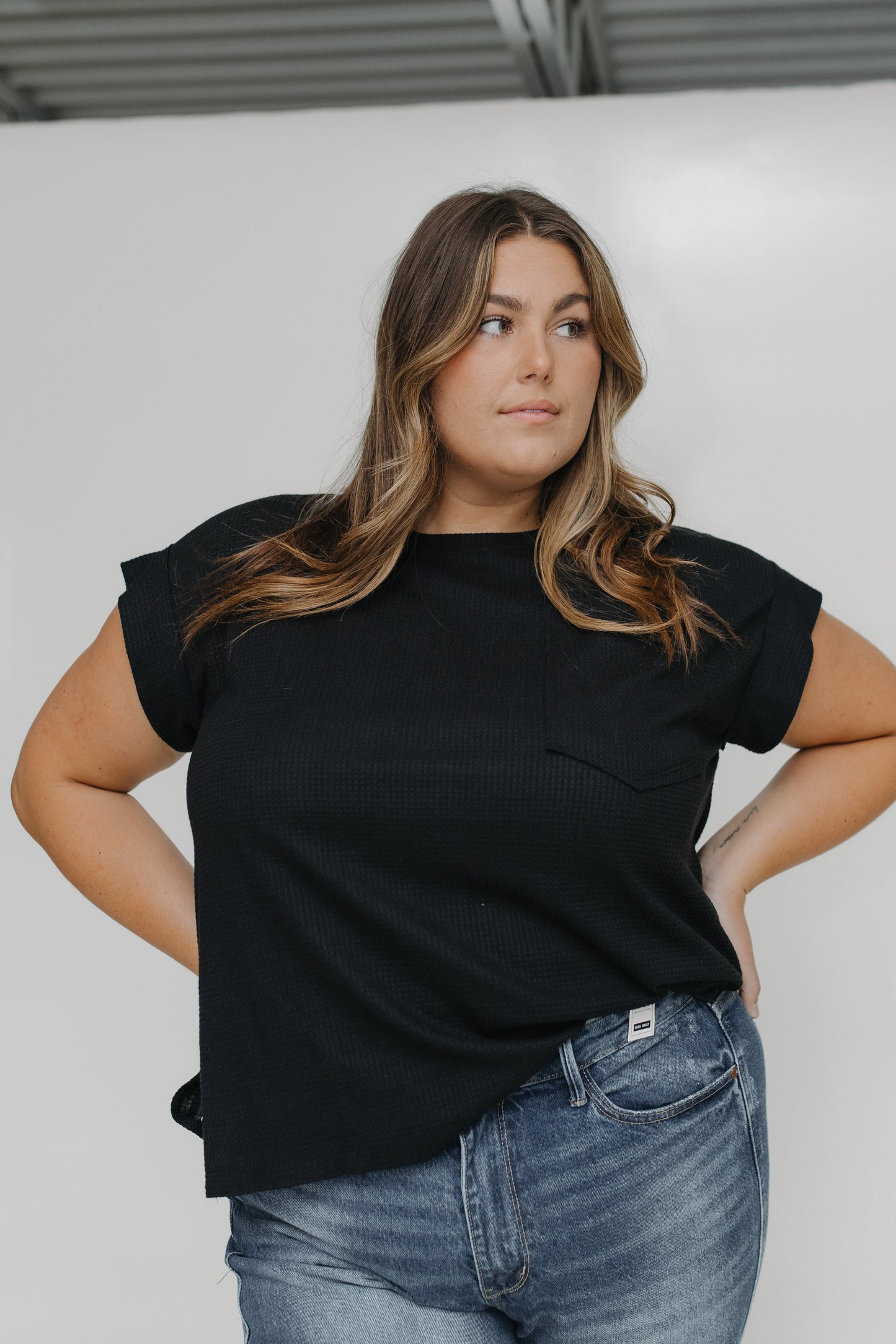 Woman wearing a black t-shirt and blue jeans against a white background