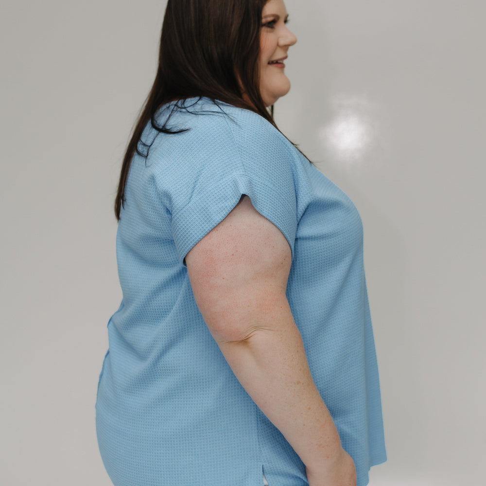 Woman wearing a light blue shirt and white shorts against a plain background