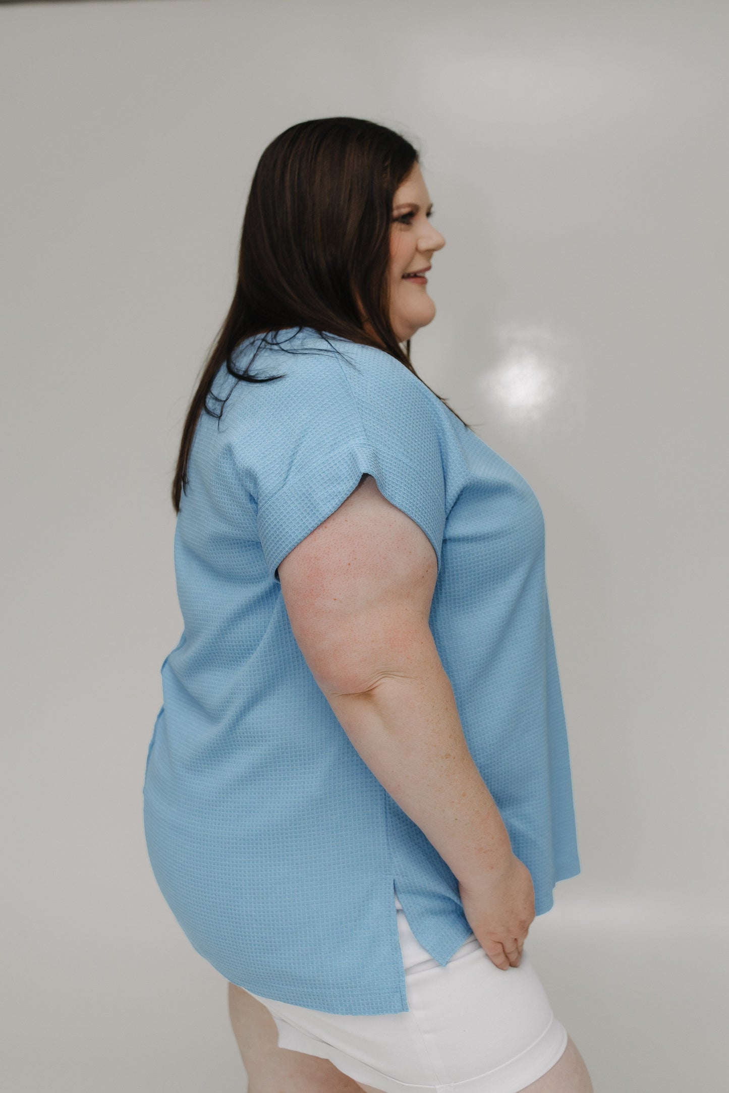 Woman wearing a light blue shirt and white shorts against a plain background