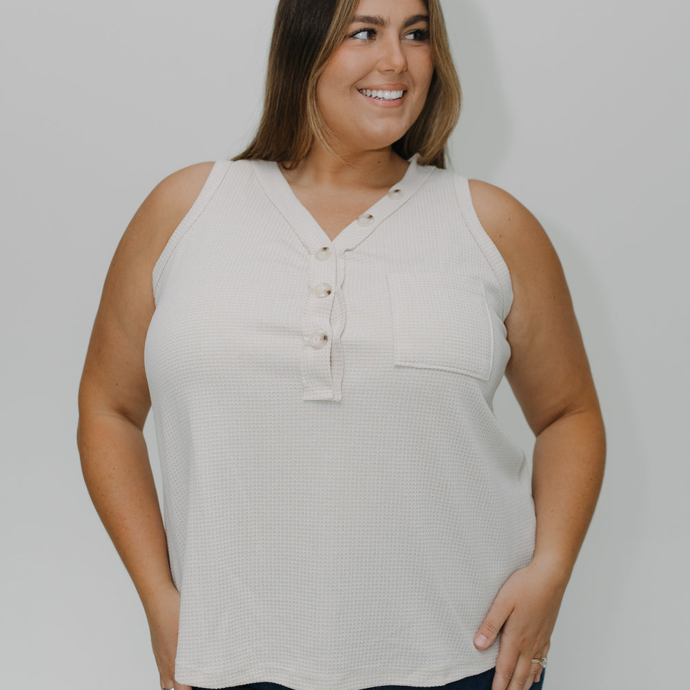 Woman wearing a beige sleeveless top and blue jeans against a plain background