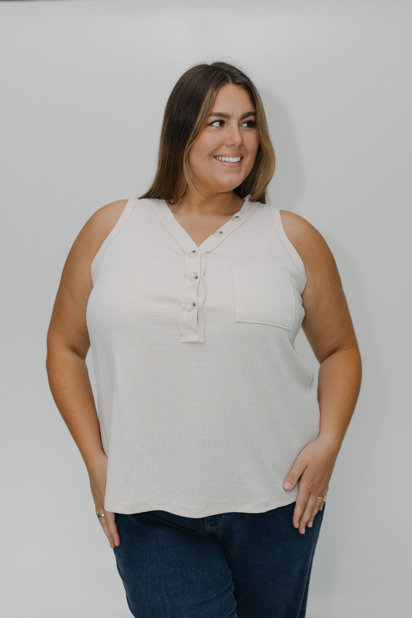Woman wearing a beige sleeveless top and blue jeans against a plain background