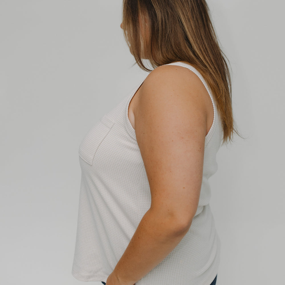 Woman wearing a white tank top and blue jeans against a plain background