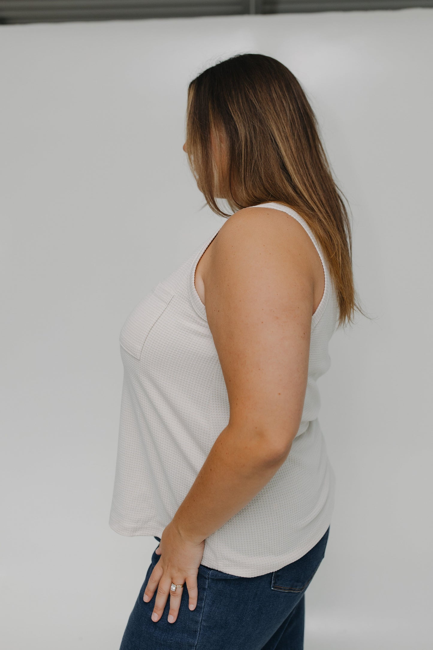 Woman wearing a white tank top and blue jeans against a plain background