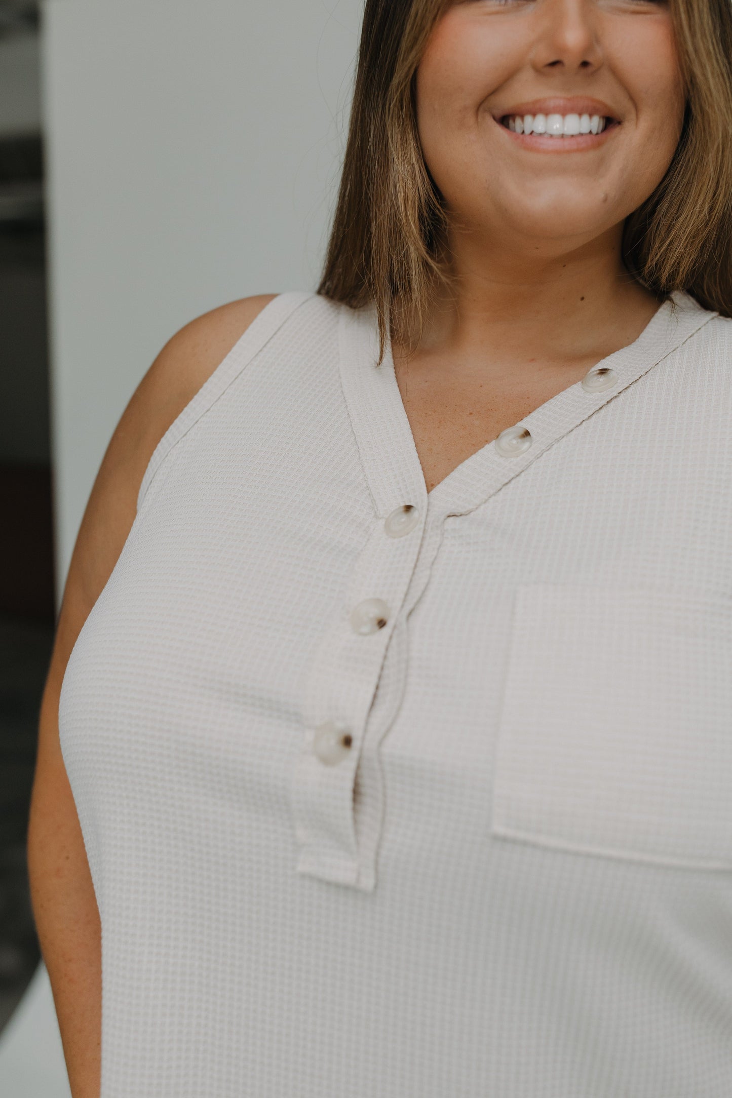 Woman wearing a beige sleeveless top with buttons, smiling outdoors.