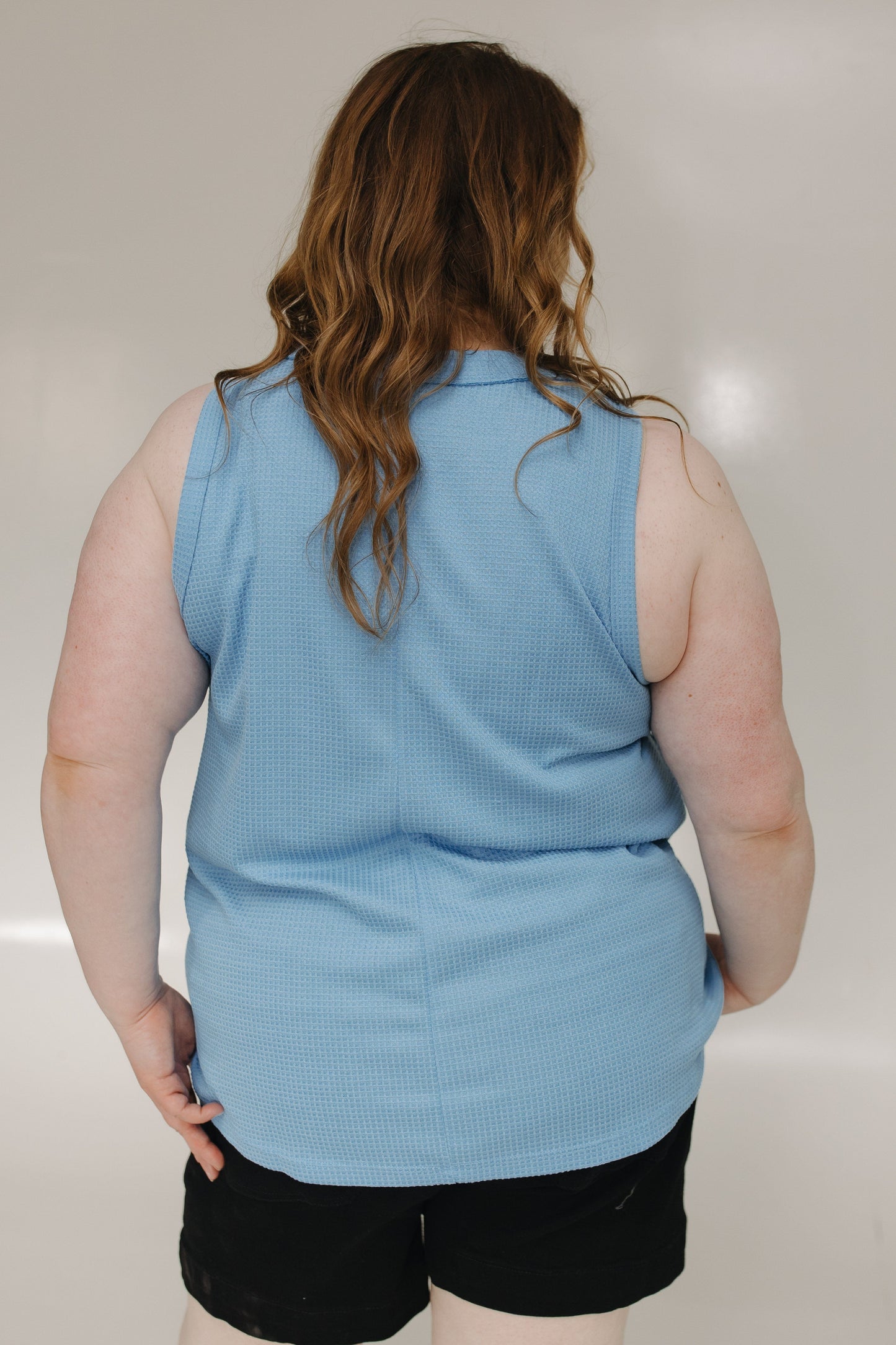 Person wearing a light blue sleeveless shirt and black shorts against a plain background