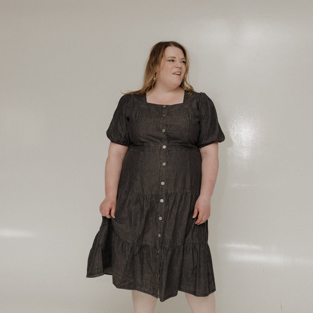Woman wearing a black dress standing against a white wall.