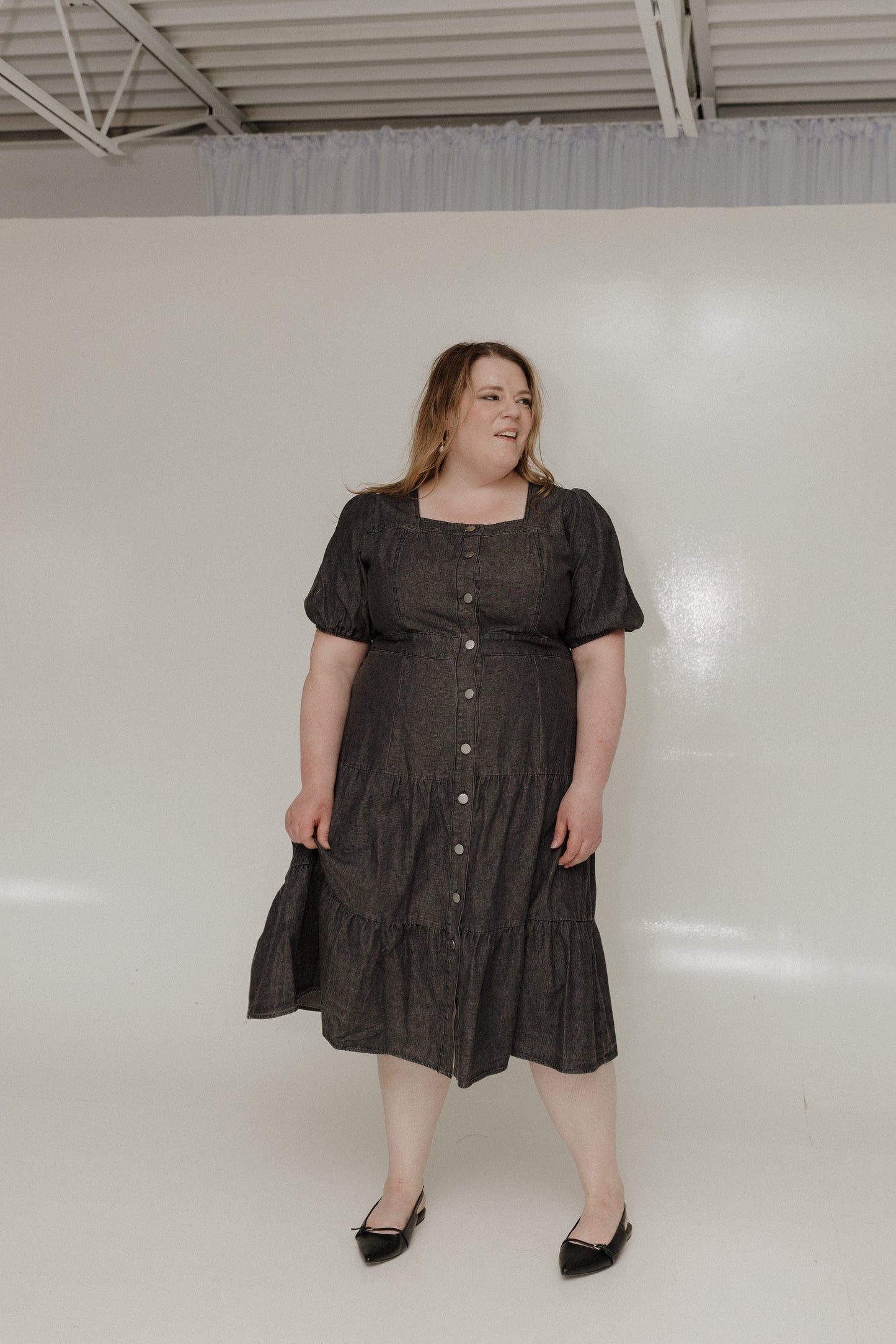 Woman wearing a black dress standing against a white wall.
