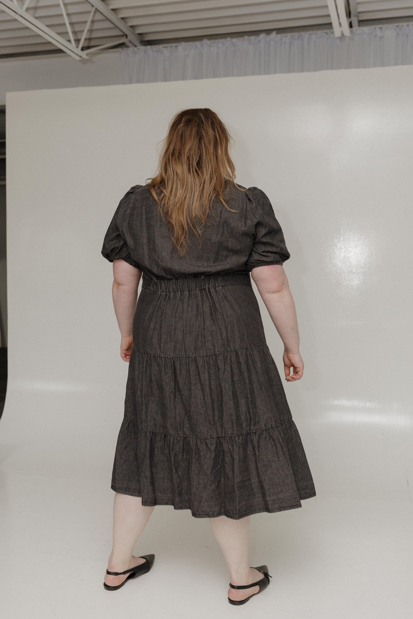 Person wearing a dark gray dress with puffed sleeves and tiered skirt on a white background