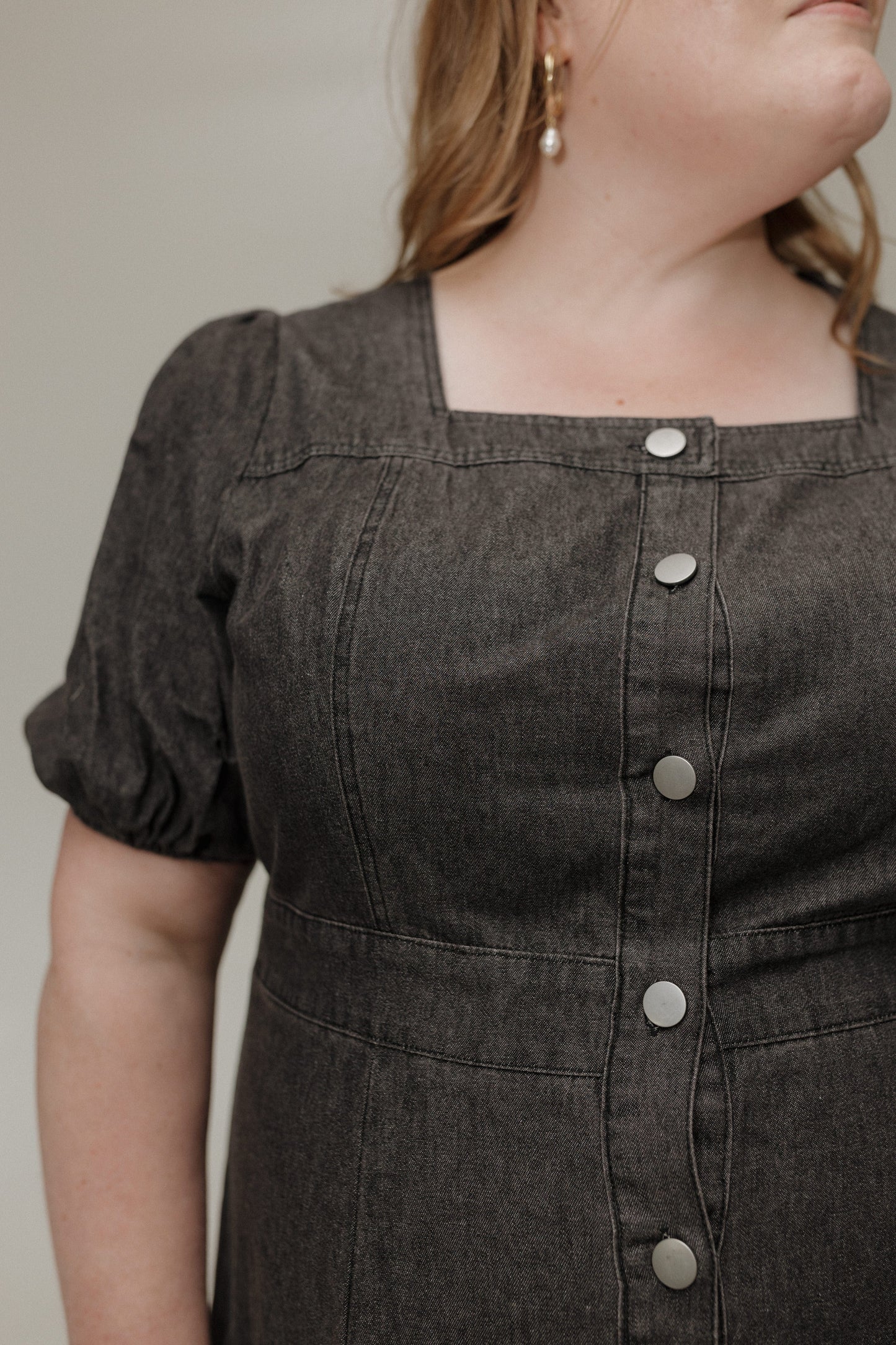 Dark denim dress with button details on a neutral background