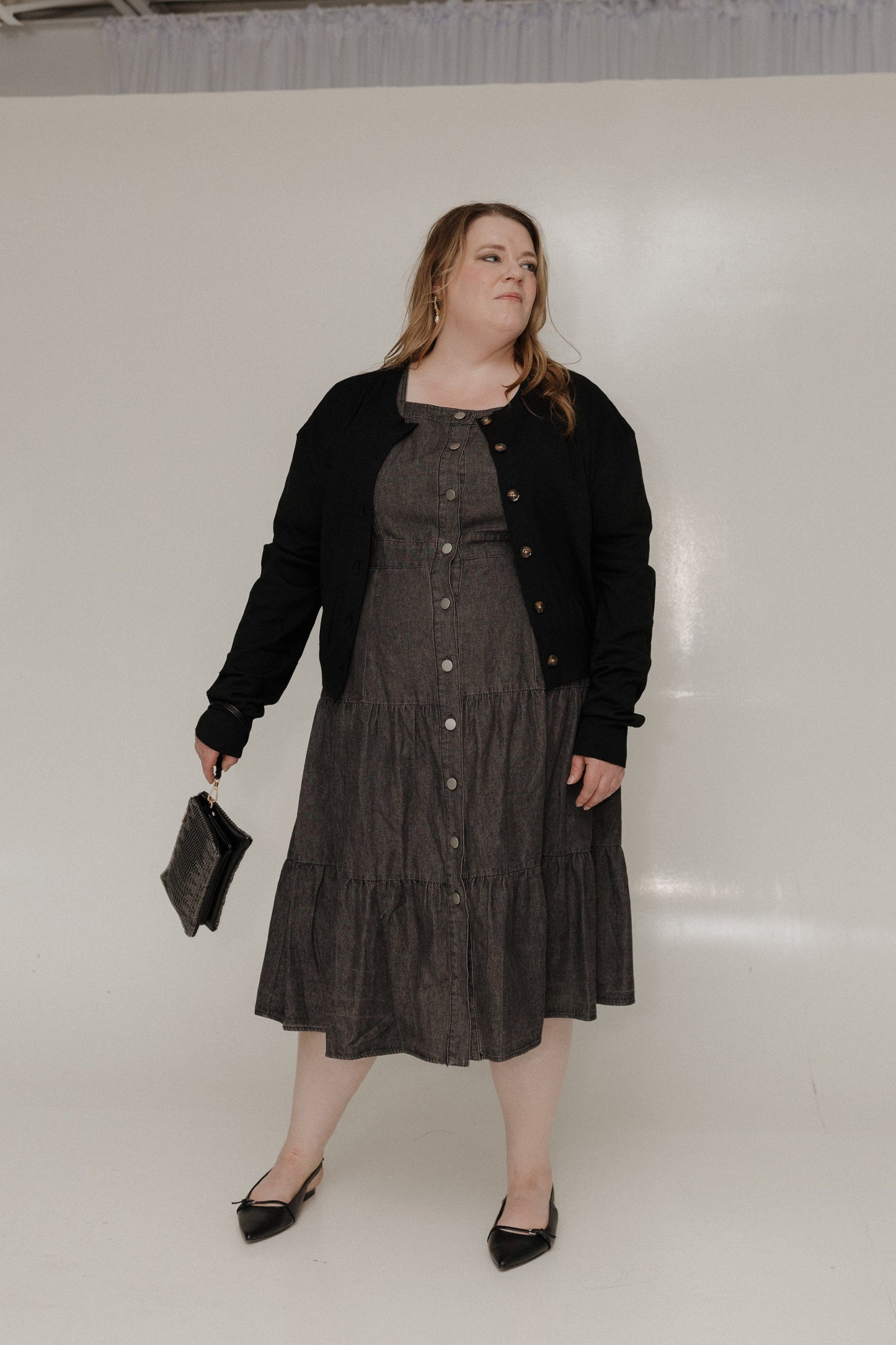 Woman wearing a black cardigan over a dark dress against a white background
