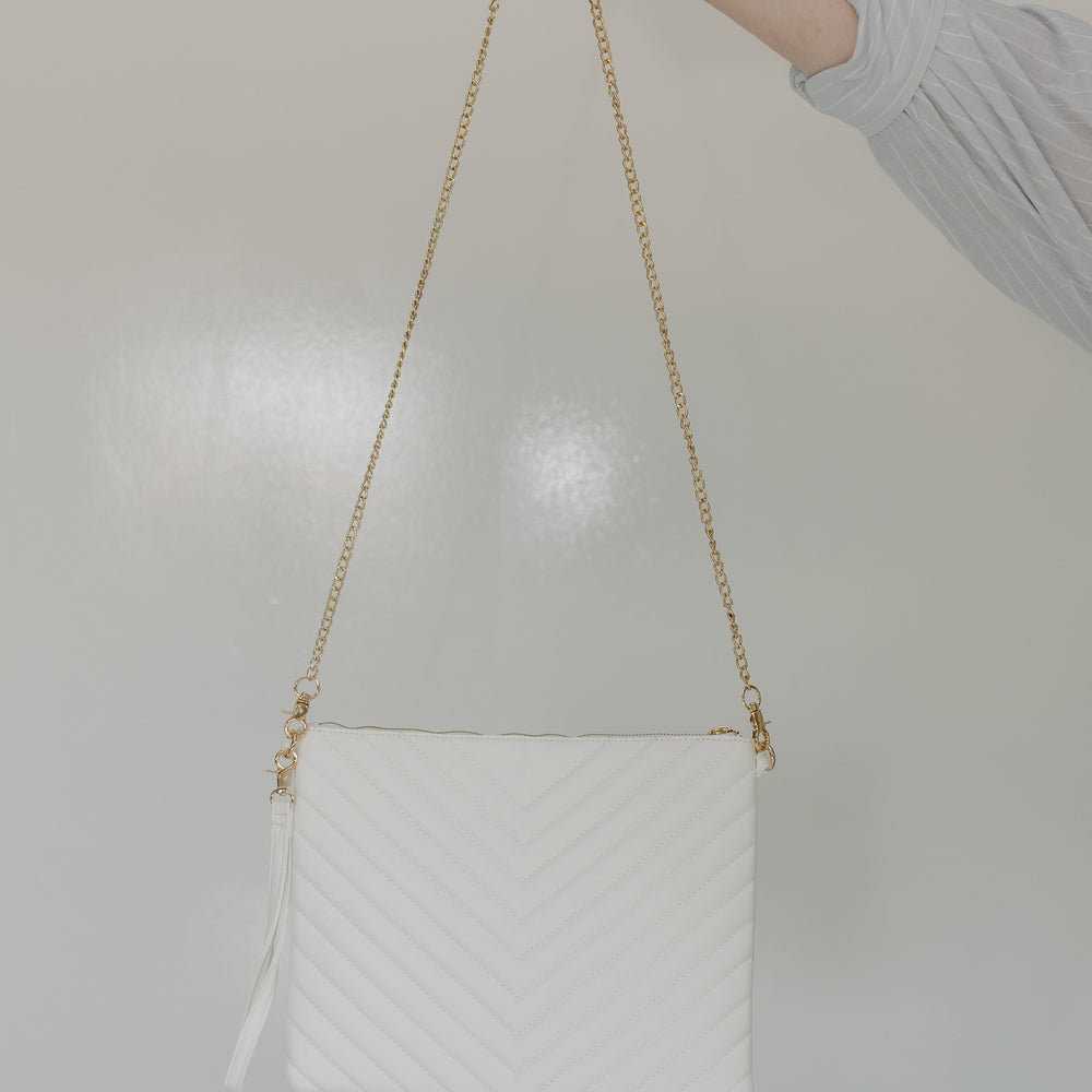White quilted handbag with a gold chain strap held by a hand against a light background